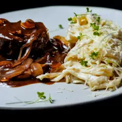 Gulasz angielski z wołowiny w sosie grzybowym, podany z kremowym makaronem tagliatelle posypanym parmezanem i kiełkami.