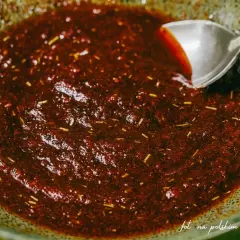Gęsta, ciemna marynata do udek z kurczaka z ziołami, gotowa do użycia. Łyżka miesza aromatyczną mieszankę.