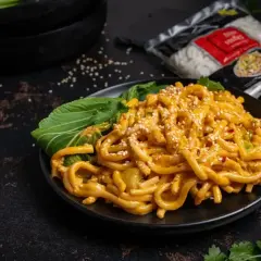 Pyszne tantanmen z grubym makaronem, polane kremowym sosem, posypane sezamem i podane z zielonymi liśćmi.