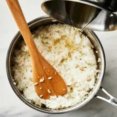 Gotowy ryż do sushi w garnku, do którego dodawany jest sos. Drewniana łyżka miesza ziarna.
