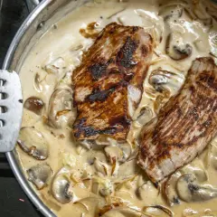 Dwa kawałki grillowanego mięsa w kremowym sosie pieczarkowym. Idealny przykład, jak zrobić sos pieczarkowy, który zachwyci smakiem.