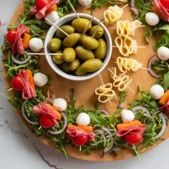 Oto 10 najlepszych sałatek na imprezę: przekąski z mozzarellą, salami, pomidorkami i oliwkami na desce.