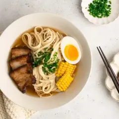 A miseczce shoyu ramen z makaronem, plastrami boczku, jajkiem na pół, kukurydzą i szczypiorkiem.