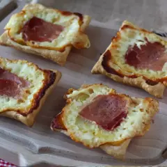 Cztery kwadratowe tartaletki z ciasta francuskiego, wypełnione roztopionym serem i plastrami szynki. Idealne na szybką przekąskę w stylu raclette.