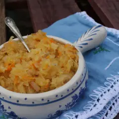Miseczka zasmażanej kapusty kiszonej z marchewką, podana na niebieskiej serwetce z białym haftem.