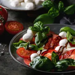 Sałatka caprese: soczyste pomidory, białe kulki mozzarelli i świeża bazylia, polane ciemnym sosem.