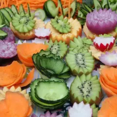 Wytworne **carving** z warzyw i owoców: kwiaty z cebuli, kiwi, marchewki, rzodkiewki i ogórka.