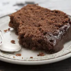Wilgotny murzynek ciasto z polewą czekoladową na talerzyku, obok srebrna łyżeczka.