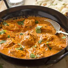 Aksamitny kurczak w sosie na bazie przyprawy curry, udekorowany świeżą kolendrą, podany z chlebkiem naan.