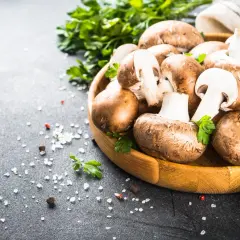 Drewniana miska z pieczarkami, natką pietruszki i solą na ciemnym tle.
