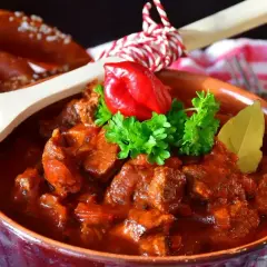 Pyszny gulasz wołowy w glinianej misce, ozdobiony papryczką chili i natką pietruszki. Idealny przepis, jak zrobić gulasz, by zachwycić bliskich.