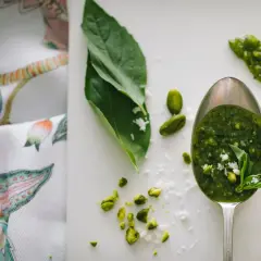 Łyżka pełna aromatycznego pesto z rukoli, obok pistacje i listki bazylii.