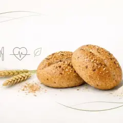 Dwie bułki grahamki posypane sezamem i siemieniem lnianym, obok kłosy zboża i garść mąki. Symbol zdrowego odżywiania.