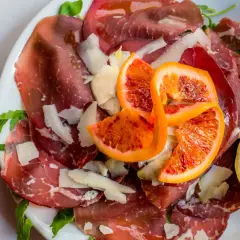 Bresaola co to? Cienkie plastry wędzonej wołowiny, parmezan, rukola i soczyste pomarańcze na talerzu.