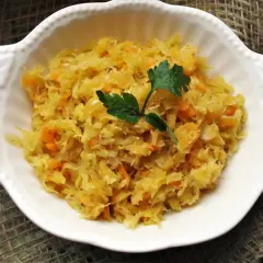 Pyszna kapusta kiszona gotowana z marchewką, udekorowana natką pietruszki, podana w białej miseczce.