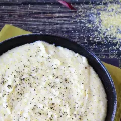 Kremowa polenta w czarnej patelni, posypana świeżo mielonym pieprzem, na drewnianym tle.