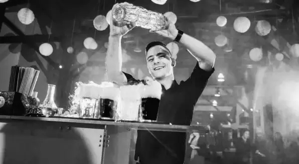 Uśmiechnięty barman z shakerem nad głową, przygotowuje drinki z dymem.