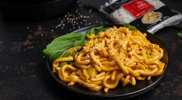 Pyszne tantanmen z grubym makaronem, polane kremowym sosem, posypane sezamem i podane z zielonymi liśćmi.