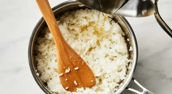 Gotowy ryż do sushi w garnku, do którego dodawany jest sos. Drewniana łyżka miesza ziarna.