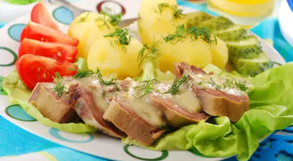 Pokrojone ozory wieprzowe w sosie, podane z ziemniakami, pomidorami i ogórkiem kiszonym.
