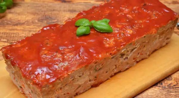 Pyszny, domowy meatloaf z sosem pomidorowym i listkami bazylii, gotowy do podania na desce.