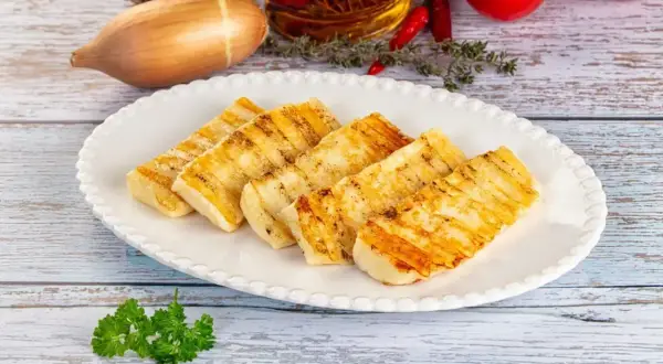 Grillowany ser halloumi na talerzu, idealny do prostych przepisów. W tle czosnek, cebula i pomidory.