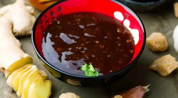 Sos teriyaki przepis: miseczka z ciemnym sosem, obok imbir, czosnek, brązowy cukier i miód.