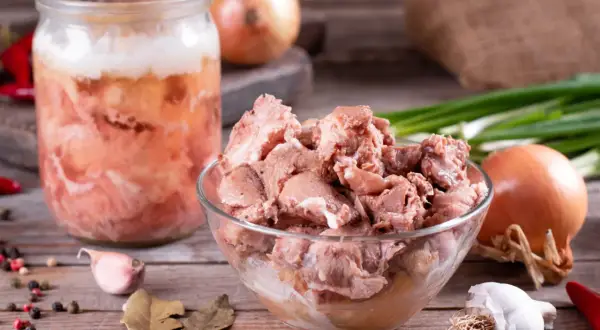 Słoik z domowym mięsem, jak u babci, pełen smaku. Obok miska z porcjami mięsa, cebula, czosnek, papryczki chili i przyprawy.
