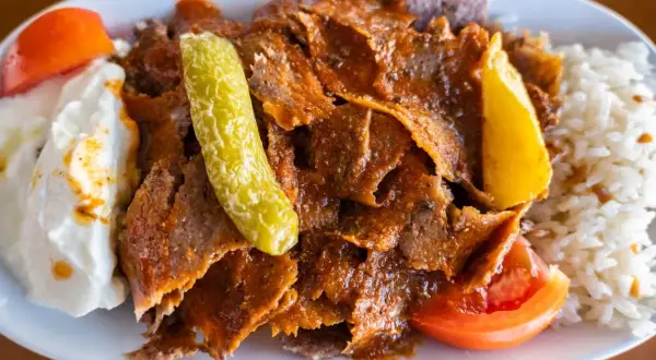 Pyszny kebab z mięsa mielonego, podany z ryżem, jogurtem, pomidorem i pikantną papryczką.