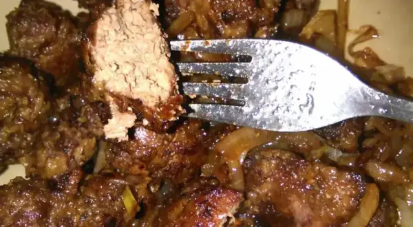 Pyszna wątróbka z cebulką, podsmażona na złoto. Widelec nabiera kawałek, by skosztować tego klasycznego dania.
