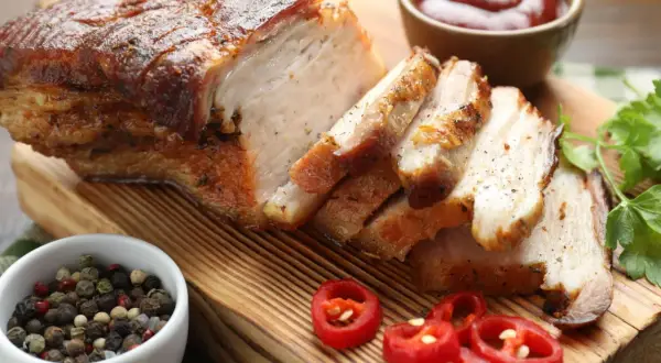 Pyszny boczek pieczony według przepisu babci Stasi, pokrojony w plastry, z dodatkiem pieprzu, chili i sosu.