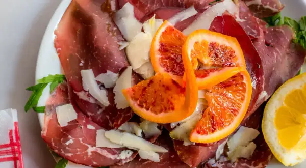 Bresaola co to? Cienkie plastry wędzonej wołowiny, parmezan, rukola i soczyste pomarańcze na talerzu.