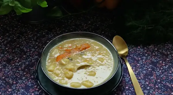 Aromaticzna zupa na żeberkach z kawałkami marchewki i ziemniaków, podana w misce obok złotej łyżki.