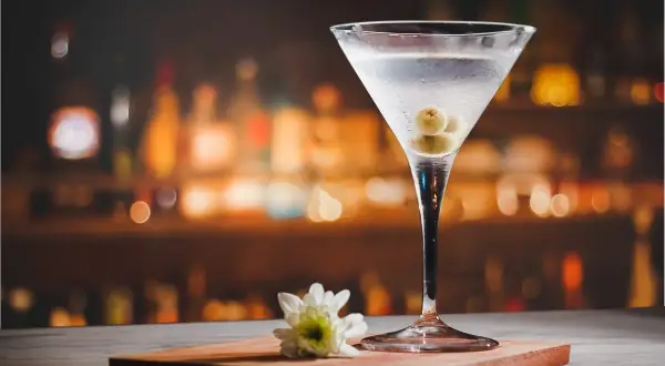 Eleganckie martini z oliwkami, idealne do delektowania się w barze. Obok biały kwiatek.