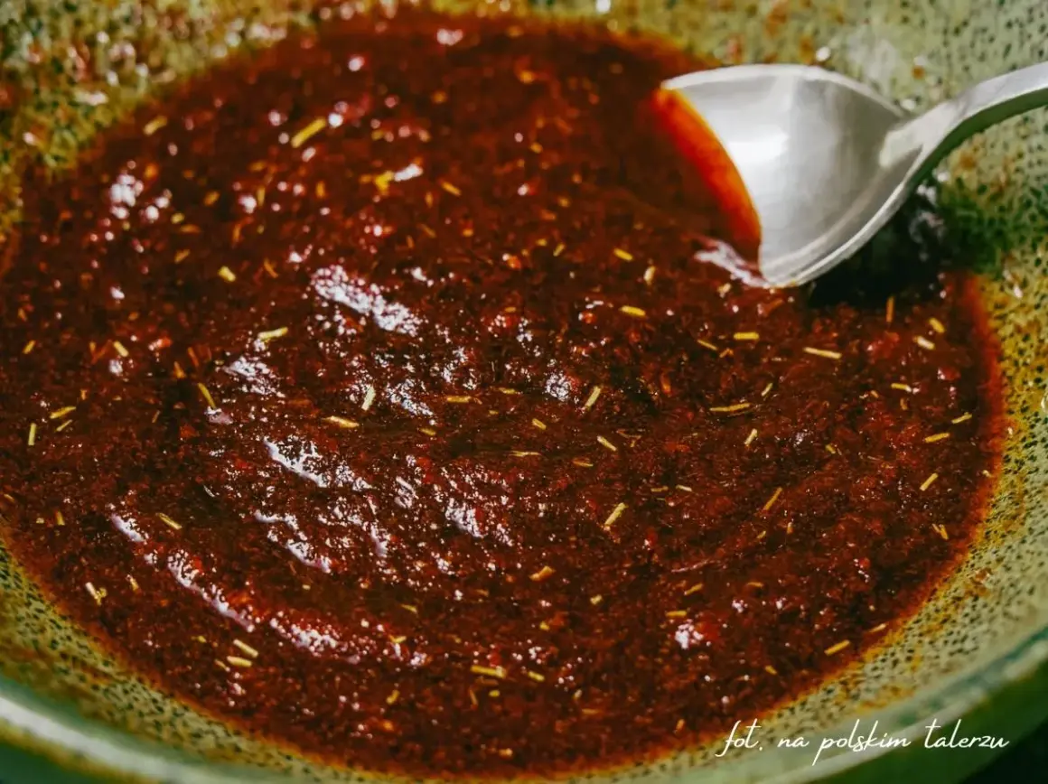 Gęsta, ciemna marynata do udek z kurczaka z ziołami, gotowa do użycia. Łyżka miesza aromatyczną mieszankę.