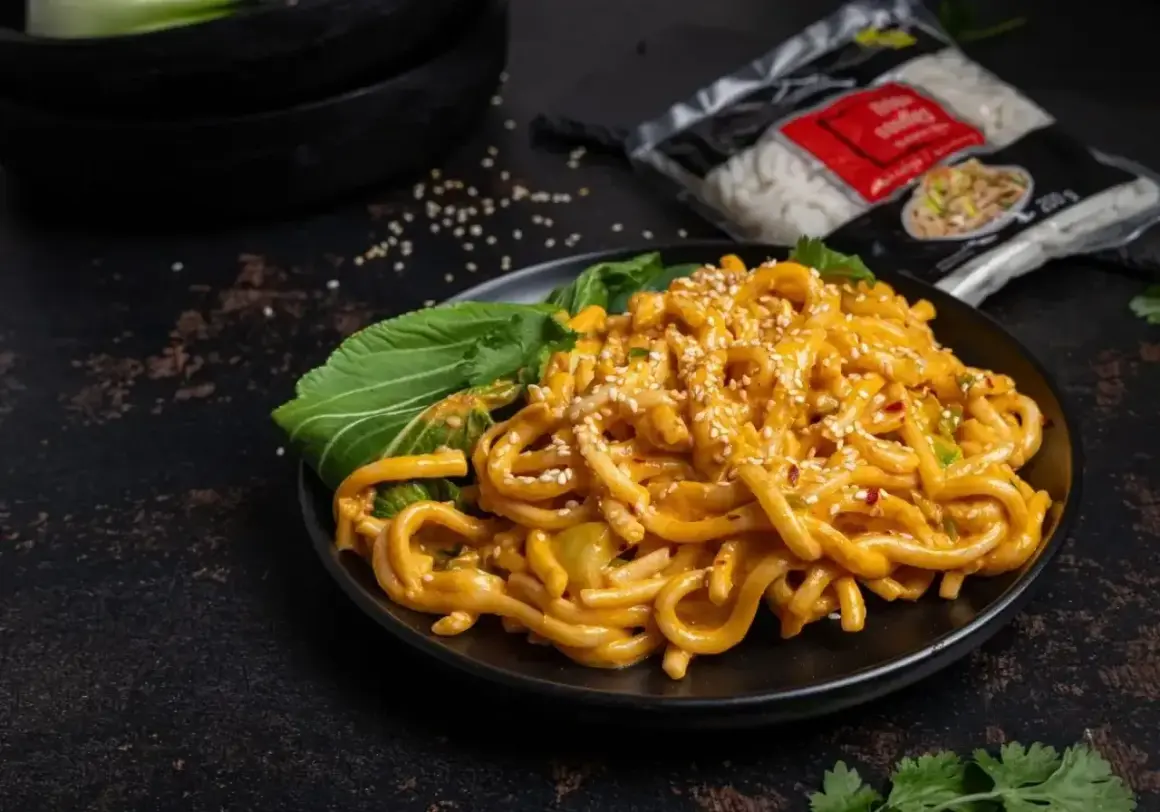 Pyszne tantanmen z grubym makaronem, polane kremowym sosem, posypane sezamem i podane z zielonymi liśćmi.