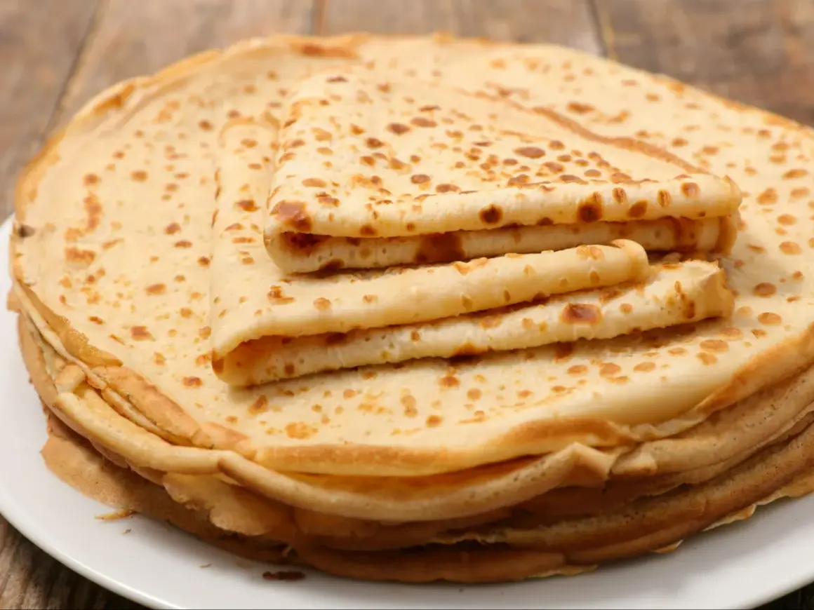 Stos klasycznych ciast na naleśniki, lekko zrumienionych, ułożonych na białym talerzu. Idealne na śniadanie.