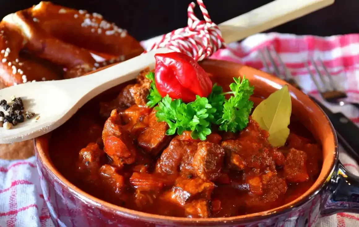 Pyszny gulasz wołowy w glinianej misce, ozdobiony papryczką chili i natką pietruszki. Idealny przepis, jak zrobić gulasz, by zachwycić bliskich.