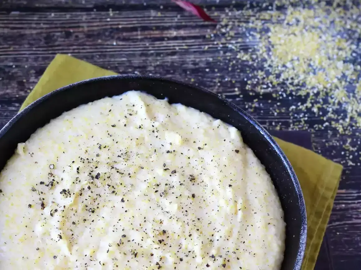 Kremowa polenta w czarnej patelni, posypana świeżo mielonym pieprzem, na drewnianym tle.