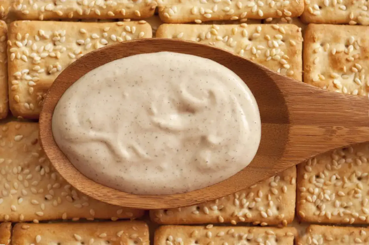 Kremowy sos na drewnianej łyżce, idealny do krakersów z sezamem. Czy to tahini? Tak, to tahini!