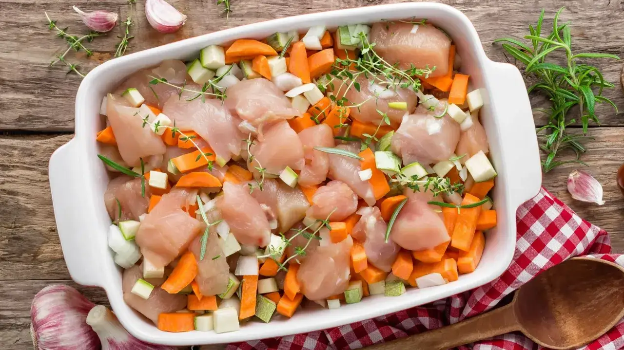 Gotowy do pieczenia filet z kurczaka z marchewką, cukinią i cebulą, doprawiony ziołami.