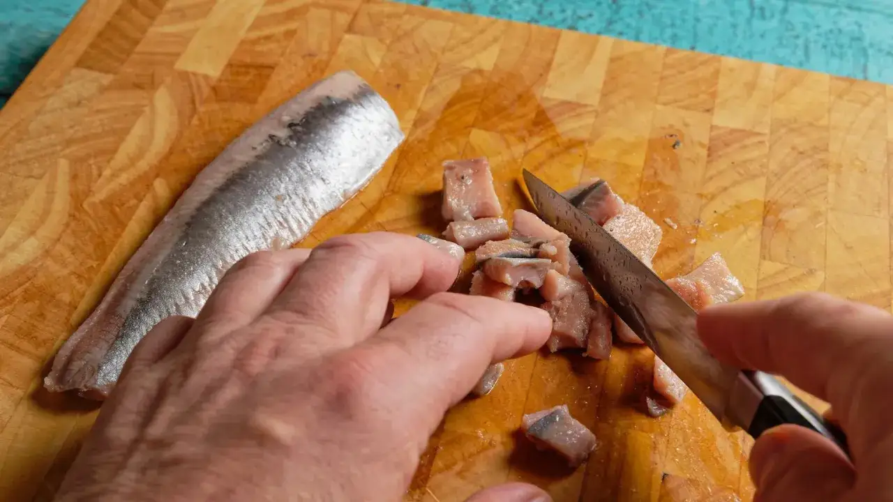 Ręce kroją na desce kawałki kiszonych śledzi. Obok leży cały filet.