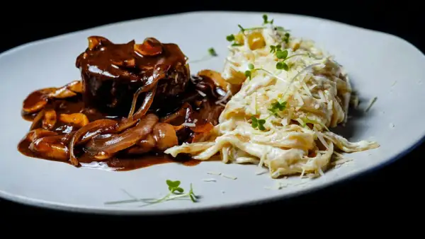 Gulasz angielski z wołowiny w sosie grzybowym, podany z kremowym makaronem tagliatelle posypanym parmezanem i kiełkami.