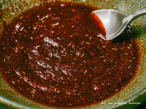 Gęsta, ciemna marynata do udek z kurczaka z ziołami, gotowa do użycia. Łyżka miesza aromatyczną mieszankę.