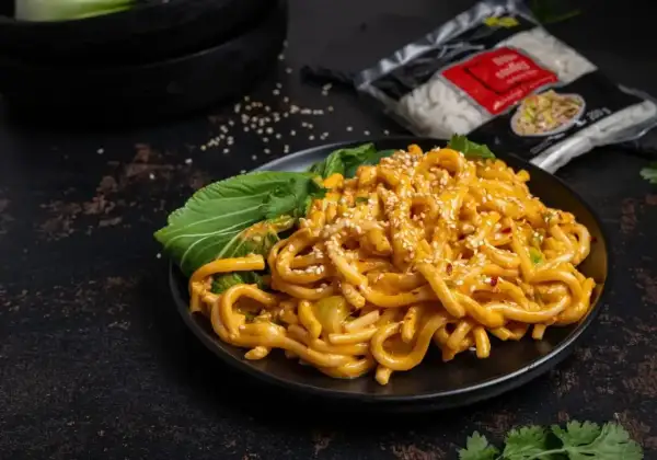 Pyszne tantanmen z grubym makaronem, polane kremowym sosem, posypane sezamem i podane z zielonymi liśćmi.
