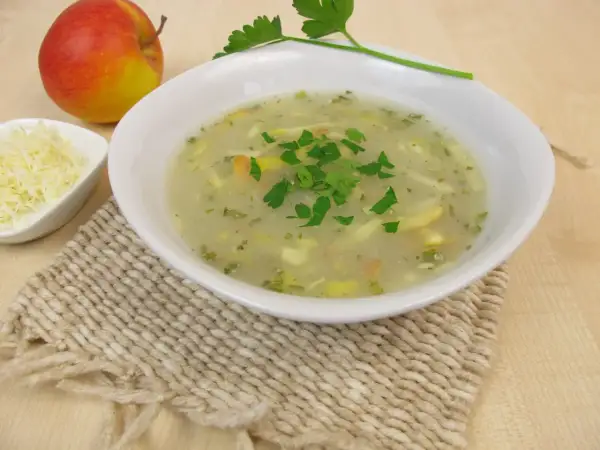Aromaticzna zupa chrzanowa z chrzanem ze słoika, udekorowana natką pietruszki, obok jabłko i starty ser.