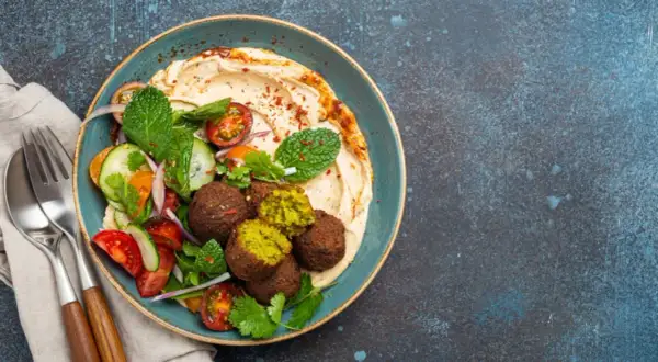 Pyszny falafel co to? Kulki z ciecierzycy z hummusem, świeżymi warzywami i miętą na talerzu.
