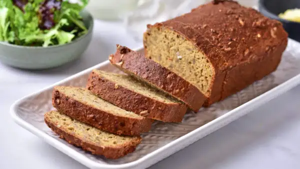 Chleb z siemienia lnianego, pokrojony na kromki, prezentuje się apetycznie obok miseczki sałatki.