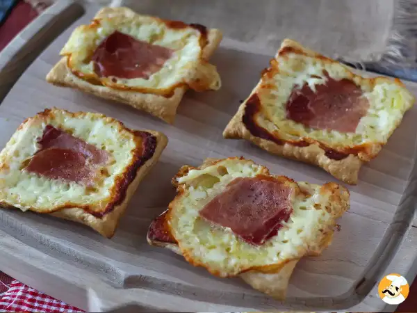 Cztery kwadratowe tartaletki z ciasta francuskiego, wypełnione roztopionym serem i plastrami szynki. Idealne na szybką przekąskę w stylu raclette.