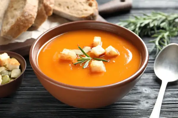 Aksamitny zupa krem z batatów, udekorowana grzankami i rozmarynem, podana z chlebem i pestkami dyni.